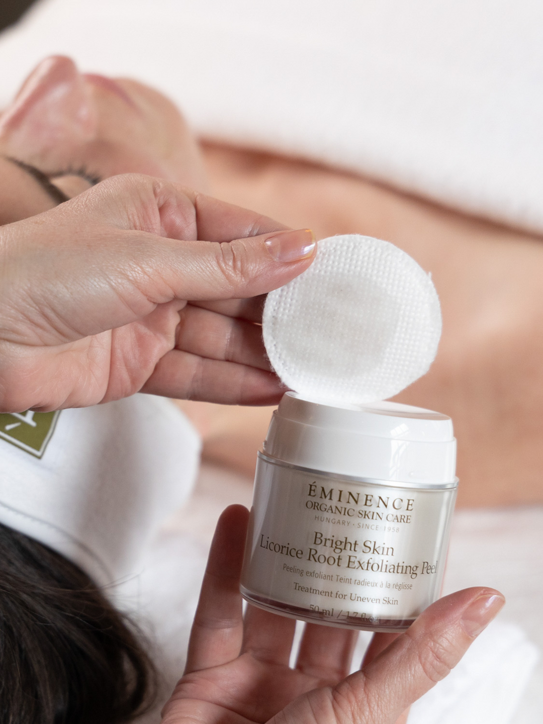 Eminence Organics Bright Skin Licorice Root Exfoliating Peel with facial client in the background