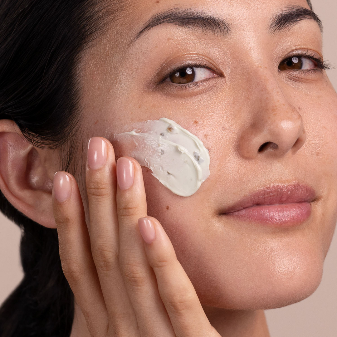 Woman applying Eminence Organics Bright Skin Masque to her face with a neutral background