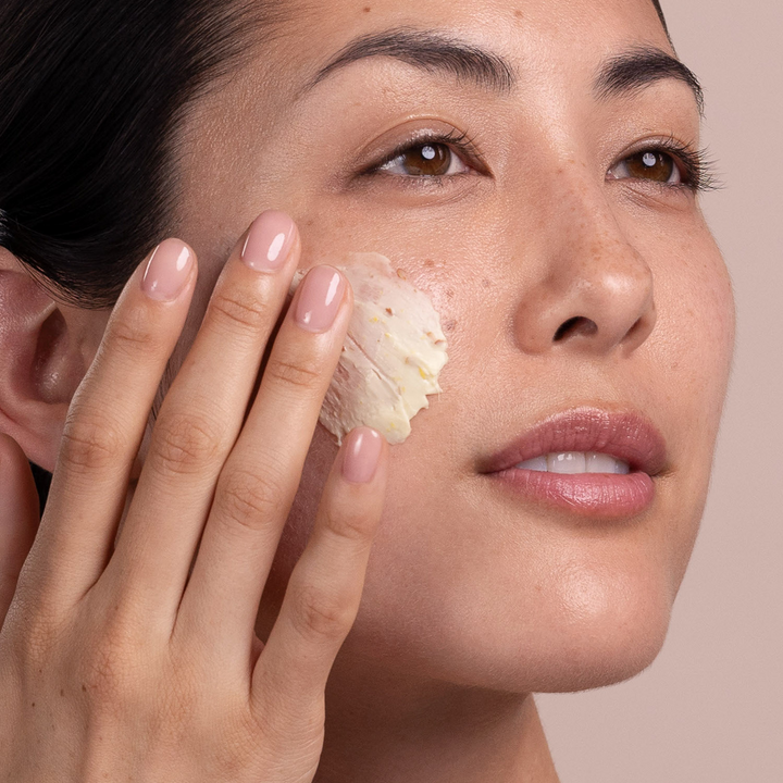Woman applying Eminence Organics Calm Skin Arnica Masque to her face with a neutral background