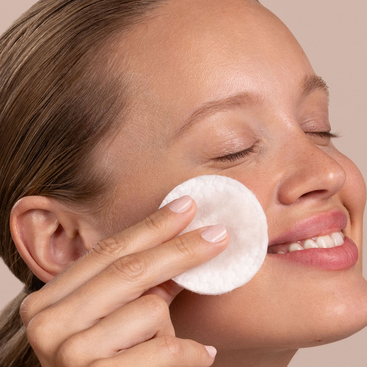 Woman applying Eminence Organics Calm Skin Chamomile Exfoliating Peel to her face against a neutral background