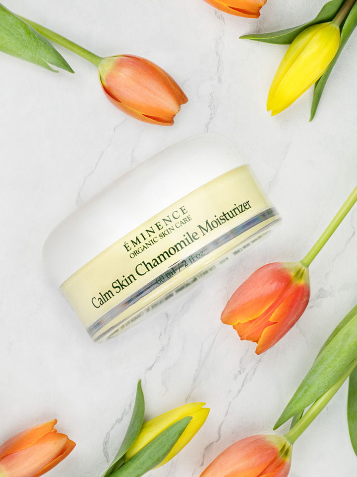 Bottle of Eminence Calm Skin Chamomile Moisturizer with tulips on a marble surface