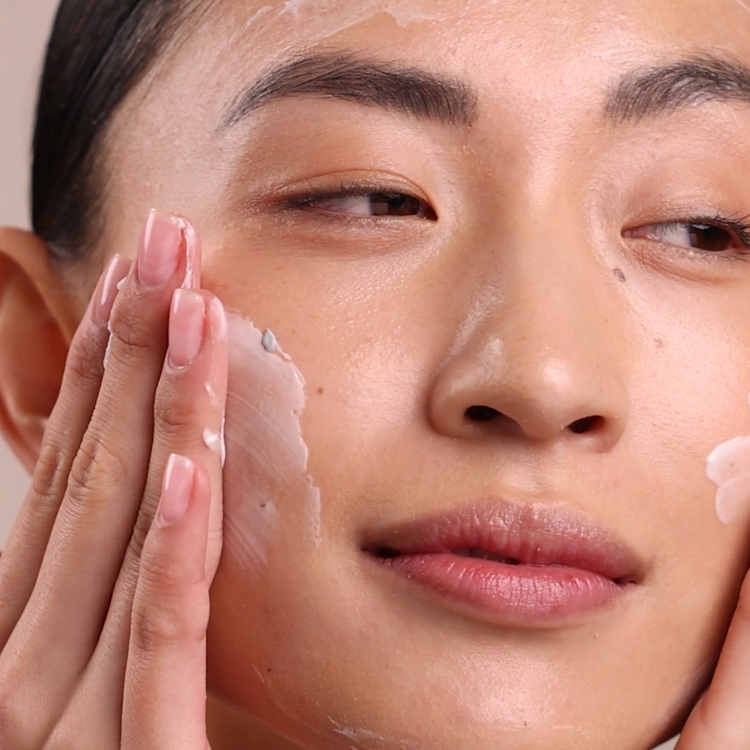 Close-up of a person applying Eminence Organics Clear Skin Probiotic Masque to their face with a neutral background