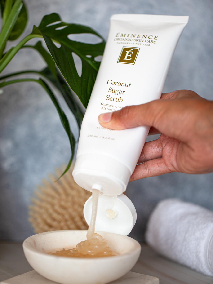 Eminence Coconut Sugar Scrub being poured into a bowl with a plant in the background