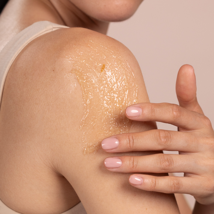 Person applying Eminence Organics Coconut Sugar Scrub to their shoulder with a hand