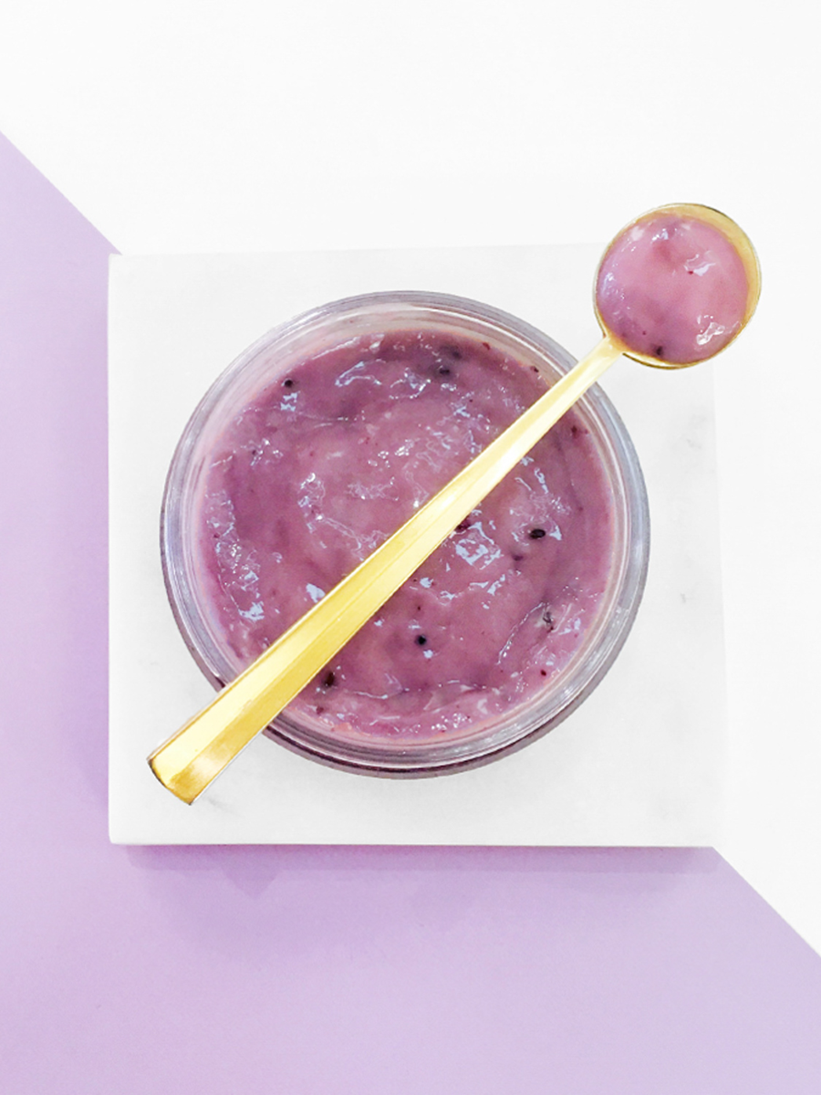 Eminence Organics Firm Skin Acai Masque a jar with a gold spoon on a light purple background