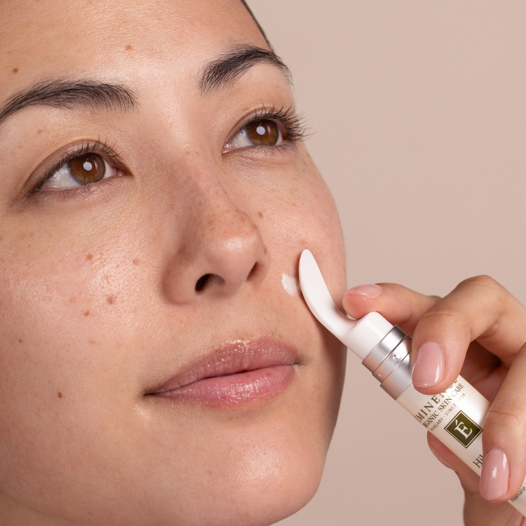 Woman applying Eminence Organics Hibiscus Instant Line Filler to her face with a beige background