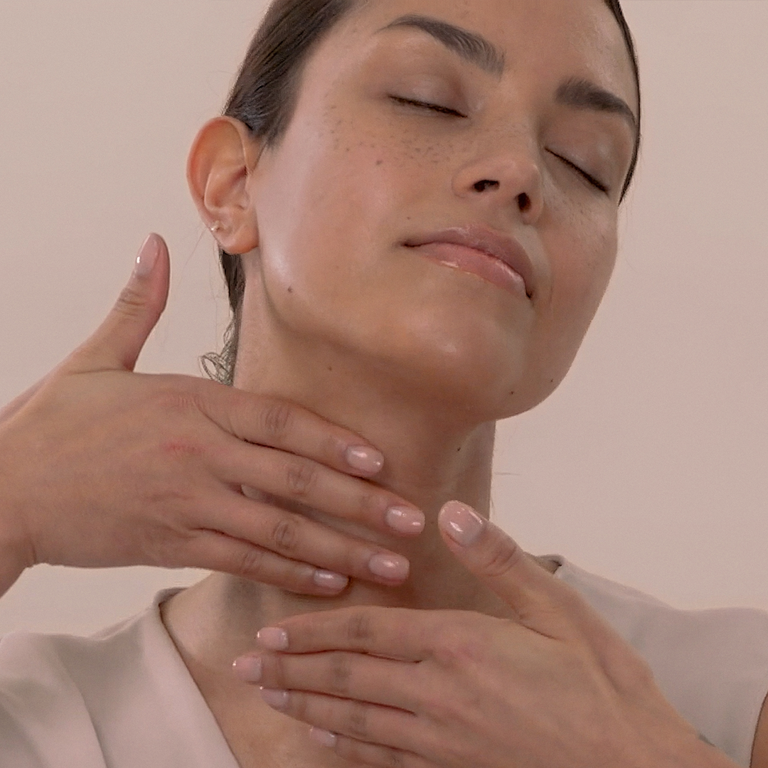 Woman with hands applying Eminence Organics Hibiscus Ultra Lift Neck Cream against a plain background