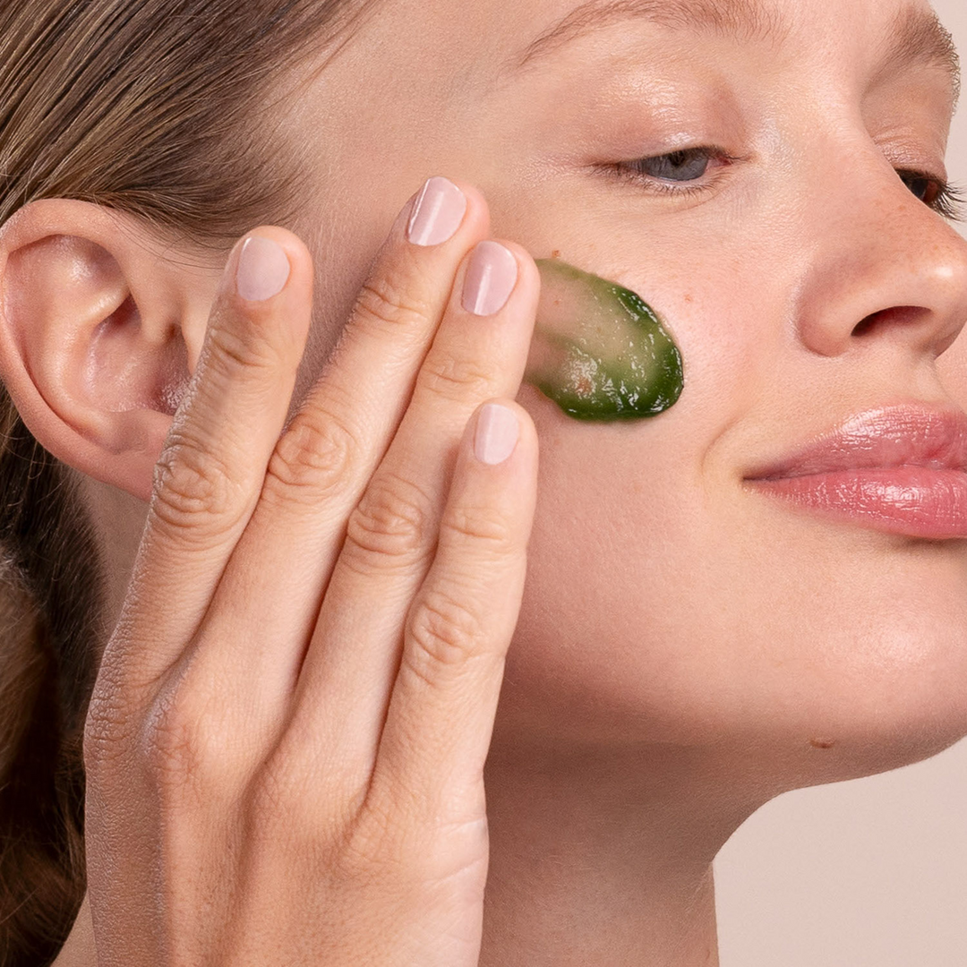 Close-up of a woman applying Eminence Organics Lime Stimulating Masque to her face.
