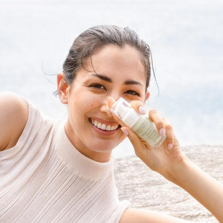 woman holding Eminence Organics Marine Flower Peptide Concentrate in her hand while on a beach