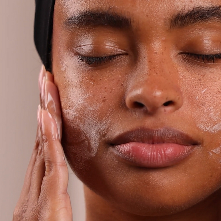 Close-up of a person applying Eminence Organics Must Have Minis Starter Set to their face with a neutral background