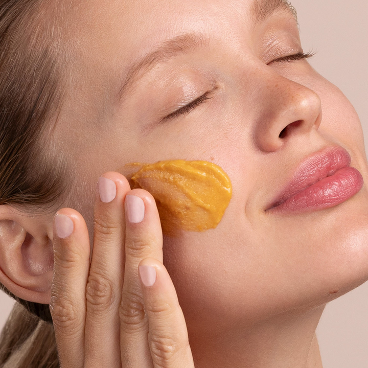 Close-up of a woman applying Eminence Organics Pumpkin Latte Hydration Masque to her face.