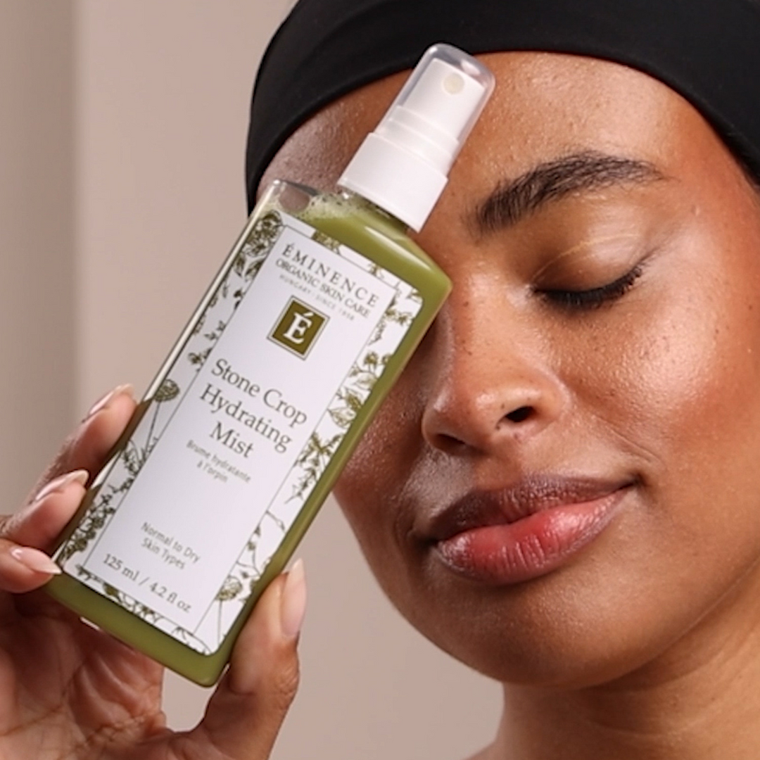 Woman holding an Eminence Organic Skin Care bottle of Stone Crop Hydrating Mist to her face.