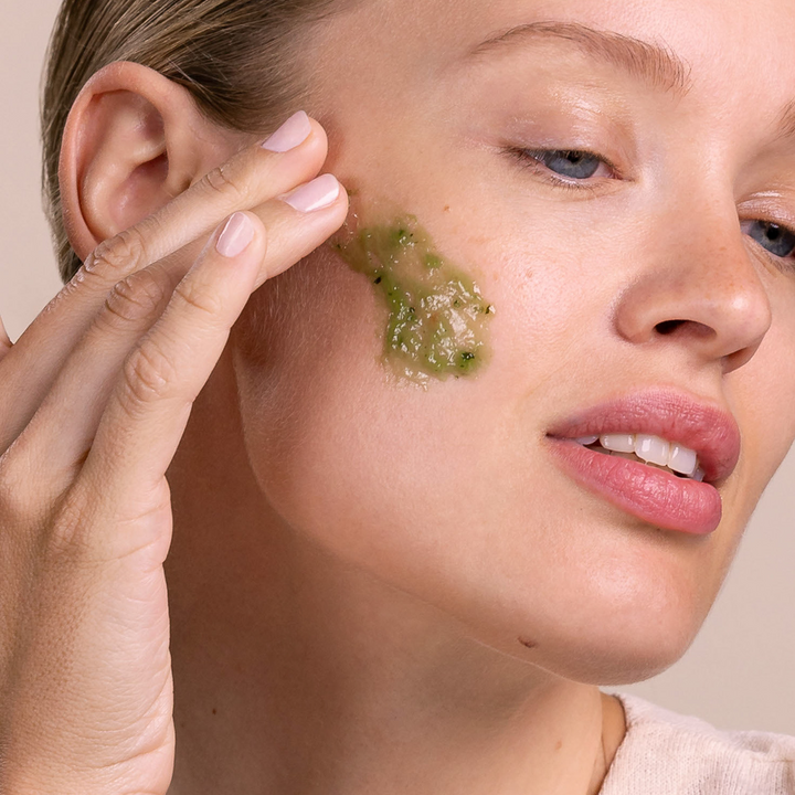 Woman applying Eminence Organics Stone Crop Masque to her cheek with a neutral background