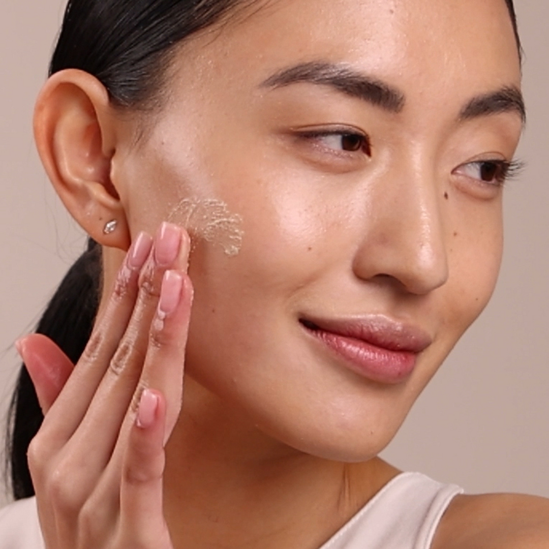 Woman applying Eminence Organics Strawberry Rhubarb Dermafoliant to her face with a neutral background