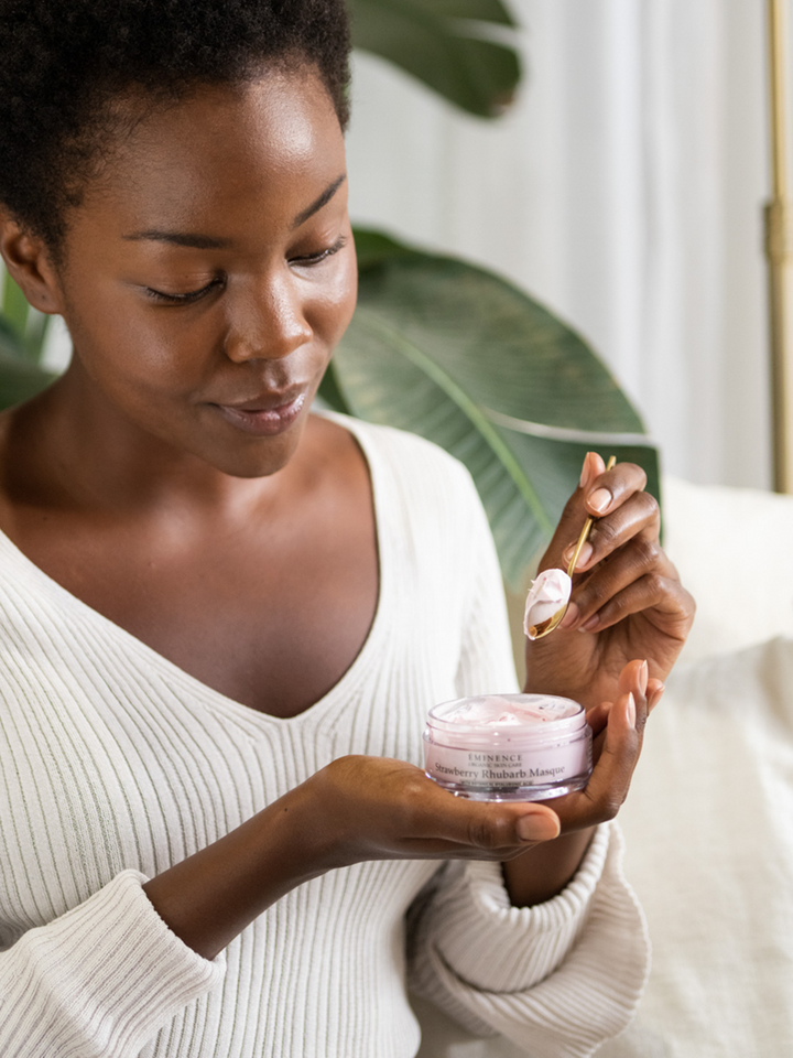 Woman holding Eminence Organics Strawberry Rhubarb Masque with a plant in the background
