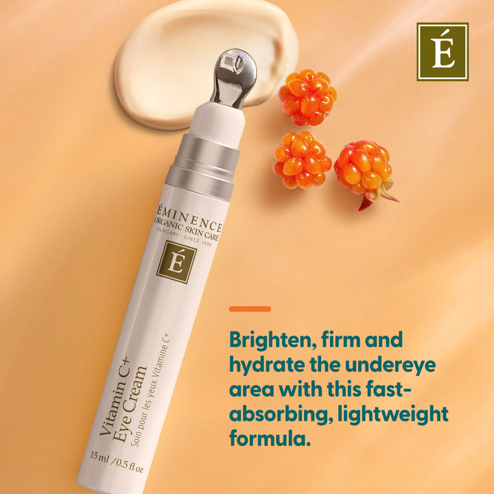 Eminence Organic Skin Care Vitamin C+ Eye Cream in a white squeeze tube with a silver applicator tip, shown on a warm peach background with a cream swatch, three orange berries, and product text.
