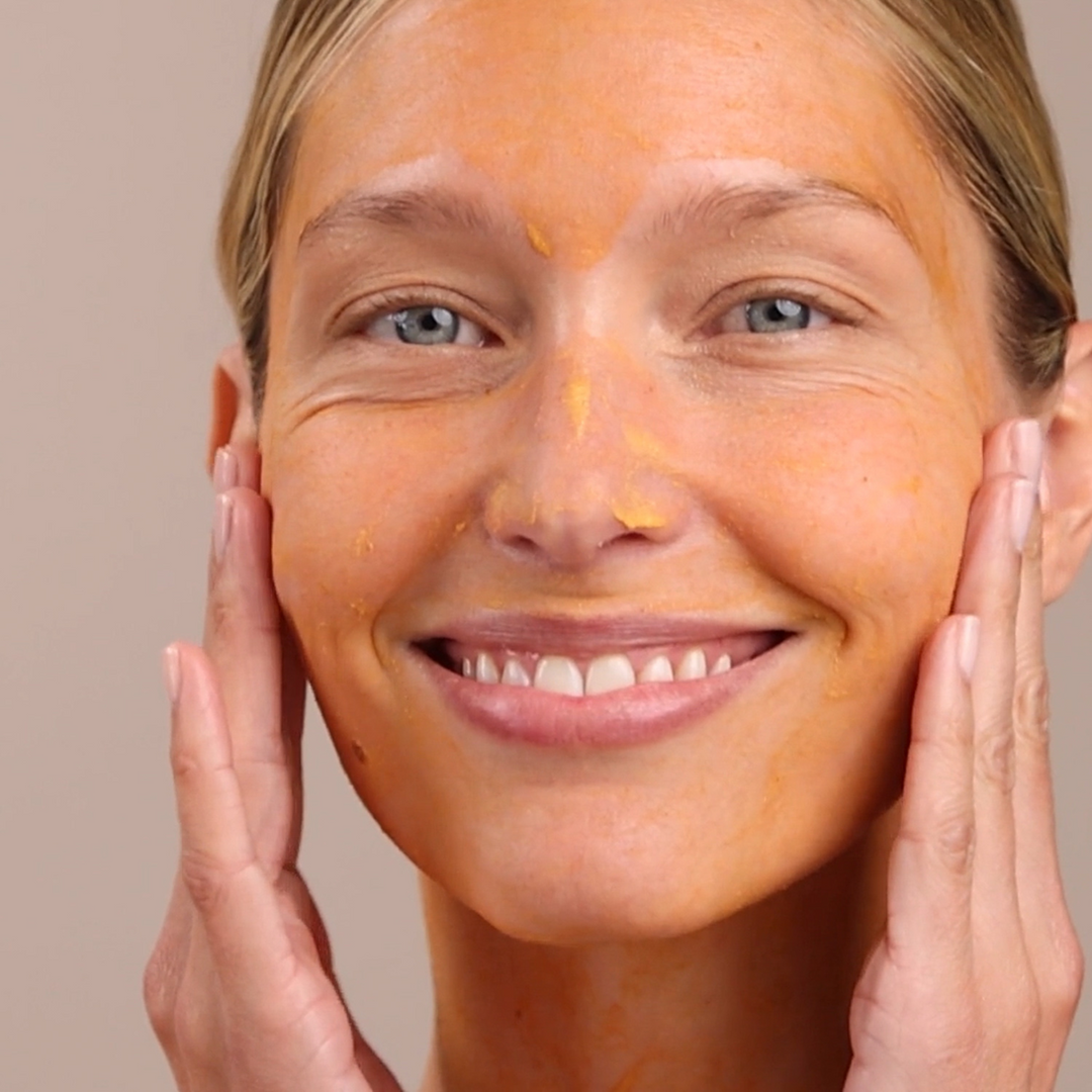 Woman applying a Eminence Organics Yam &amp; Pumpkin Enzyme Peel 5% to her face with a neutral background