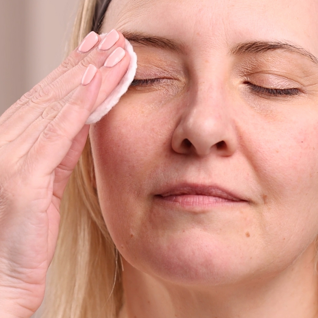 Woman cleaning her face with a cotton pad, close-up of her face.